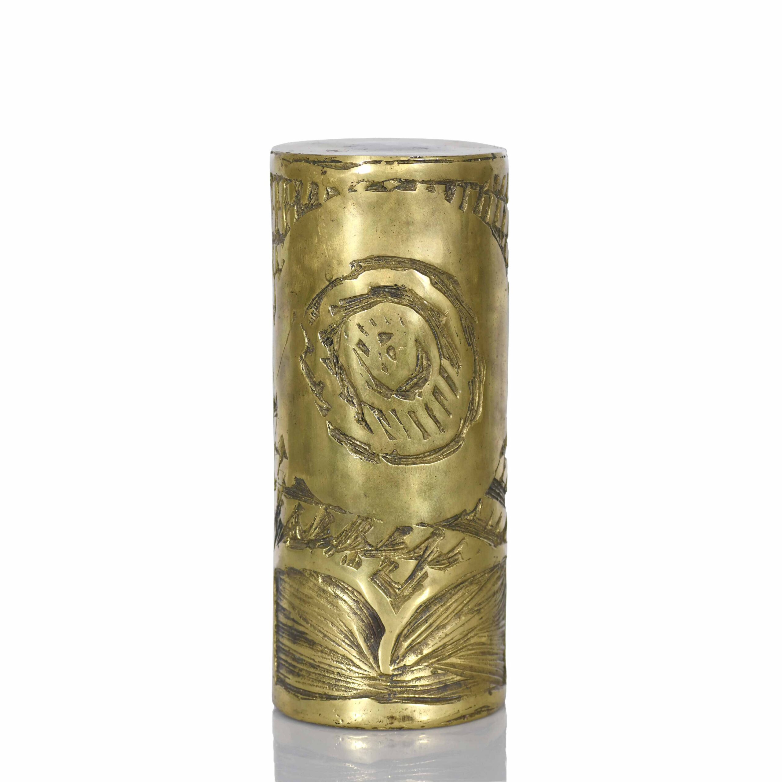 Objet cylindrique en laiton gravé avec des motifs abstraits.