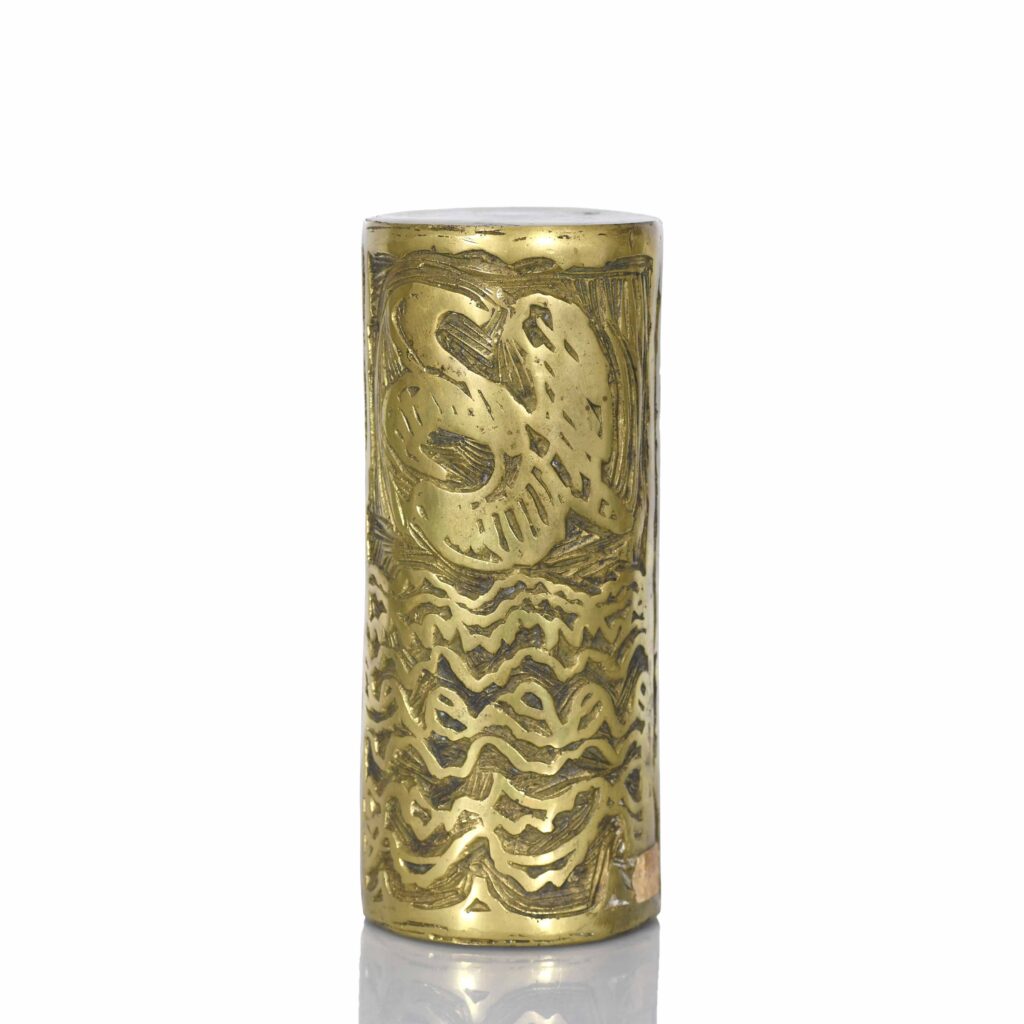 Objet cylindrique en laiton gravé avec des motifs abstraits.