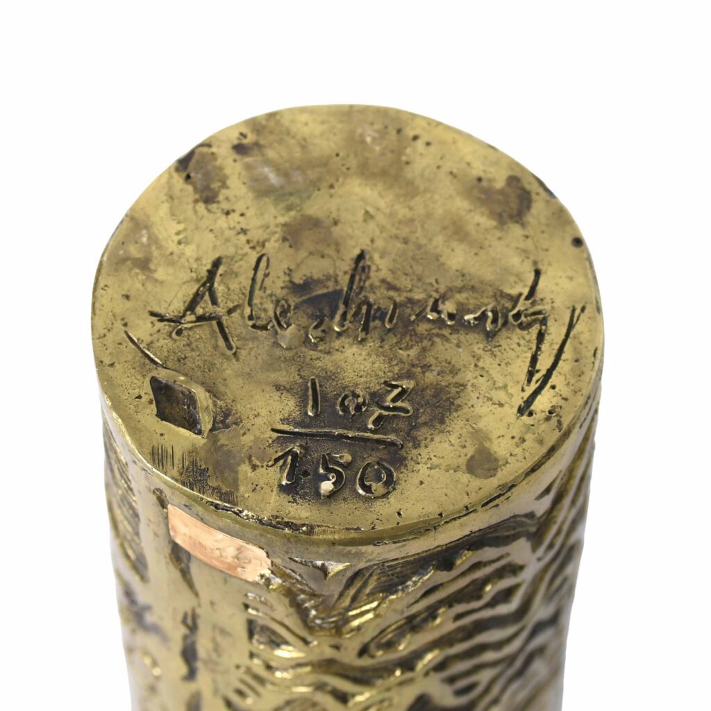 Objet cylindrique en laiton gravé avec des motifs abstraits.